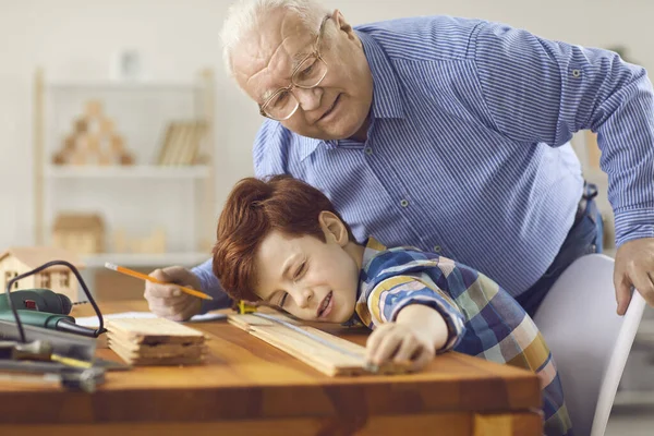 Nonno e nipote misurano la tavola di legno mentre lavorano insieme in falegnameria — Foto Stock