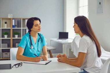 Genç doktor, klinikteki kadın hastayı dinliyor.