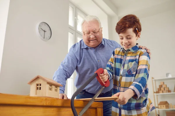 Sorridente nipotino segare una tavola di legno mentre suo nonno sta guardando — Foto Stock