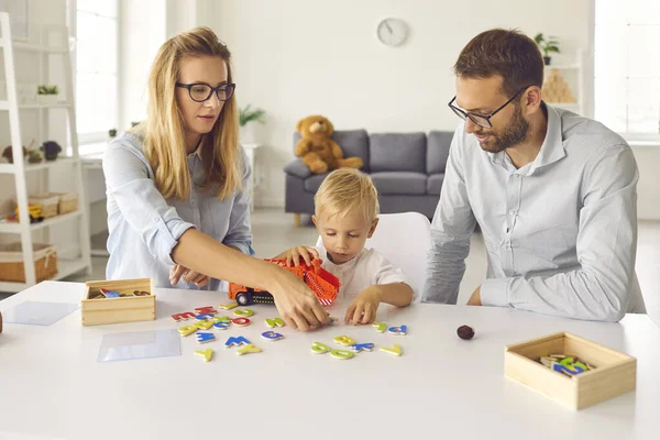 Focada mãe, pai e filho criança jogar e compor palavras de letras coloridas dispersas. — Fotografia de Stock