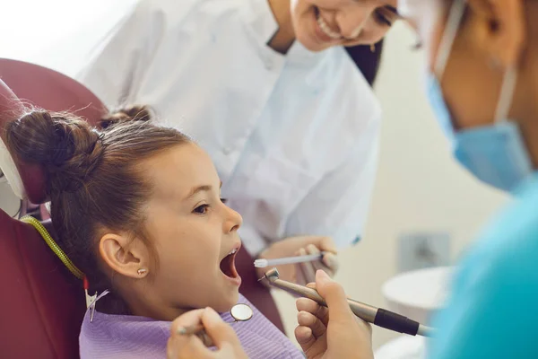 Klein meisje liggend in een tandartsstoel en grijnzend, niet bang voor een mondholte onderzoek. — Stockfoto