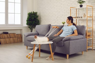 Kırık bacağı alçılı genç bir kadın evdeki kanepede oturup düşünüyor.