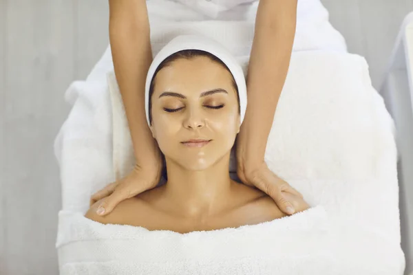 Manos de cosmetólogo haciendo masaje facial con hombros para sonreír mujer serena —  Fotos de Stock