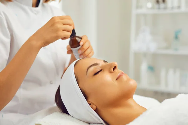 Hands of therapist ready to put nourishing skin oil to young womans face during skincare procedure — Stock Photo, Image