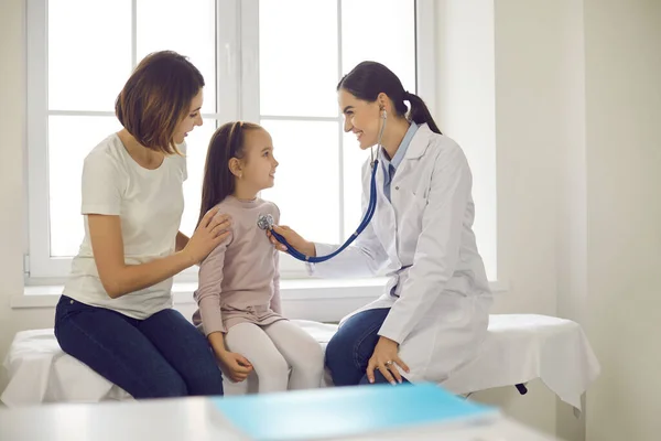 Amistoso médico que escucha a pequeños pacientes respirar o latidos del corazón durante el chequeo médico —  Fotos de Stock