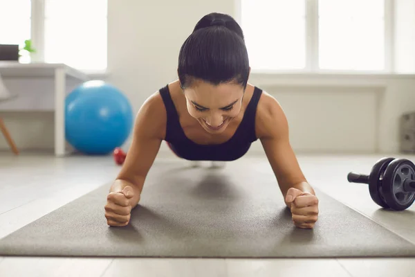 Gericht glimlachende vrouw houden plank en het doen van oefeningen op buikspieren in heldere sportschool. — Stockfoto