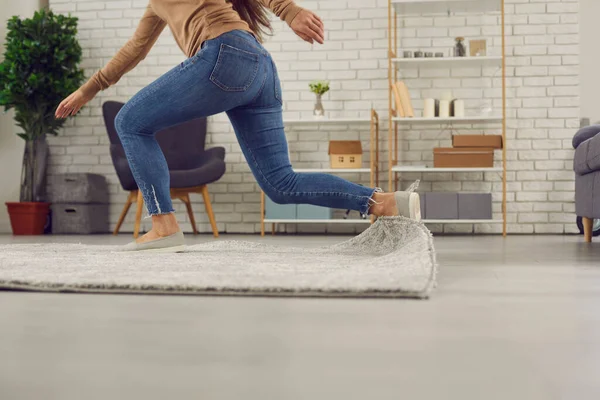 Onhandige vrouw struikelt op het tapijt in de woonkamer en valt neer op de vloer — Stockfoto