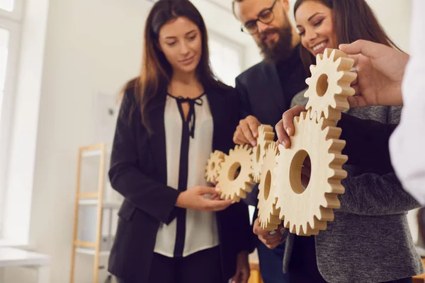 Business people stand in a row and put together wooden gear forming the mechanism of their work.