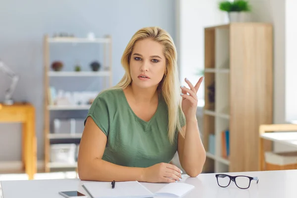 Seriöse junge Frau sitzt am Schreibtisch, diskutiert über Arbeitsfragen und teilt ihre Meinung — Stockfoto