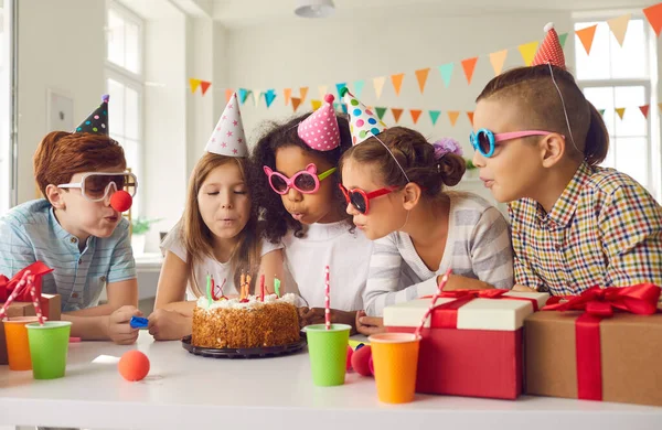 Bir grup çocuk doğum günü pastasında mum üfleyerek evde eğleniyorlar. — Stok fotoğraf