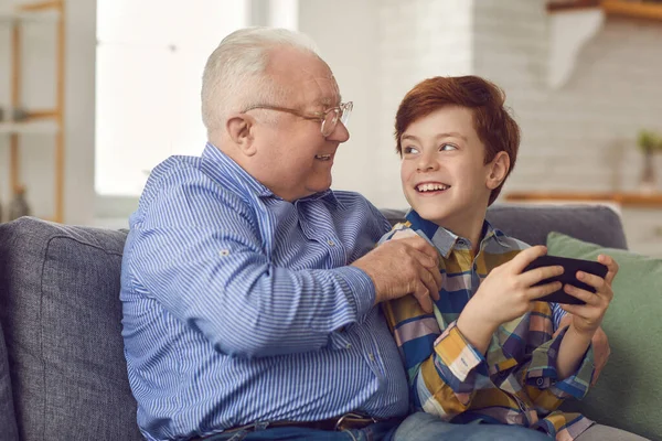 Heureux petit-fils et grand-père assis sur le canapé et jouer à des jeux sur un nouveau téléphone mobile — Photo