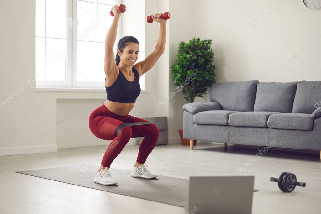 Home online workout in front of a laptop with dumbbells and sports rubber bands.