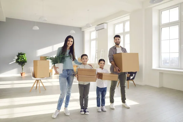 Feliz familia sonriente con niños que llevan cajas de cartón mientras se mudan a un nuevo hogar — Foto de Stock