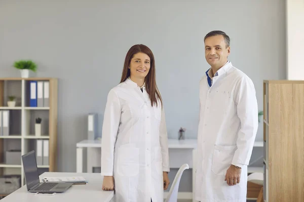 Trabajadores médicos sonrientes con batas blancas de laboratorio de pie juntos en la oficina del hospital moderno —  Fotos de Stock