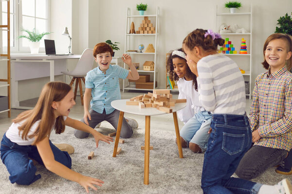 Bunch of children laughing at broken wood block tower while playing stacking board game together
