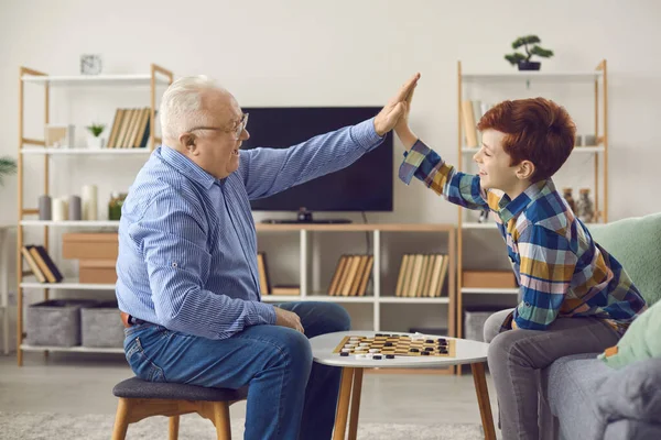 Щасливий дідусь і онук високопоставлені один одного після гри в шашки вдома — стокове фото