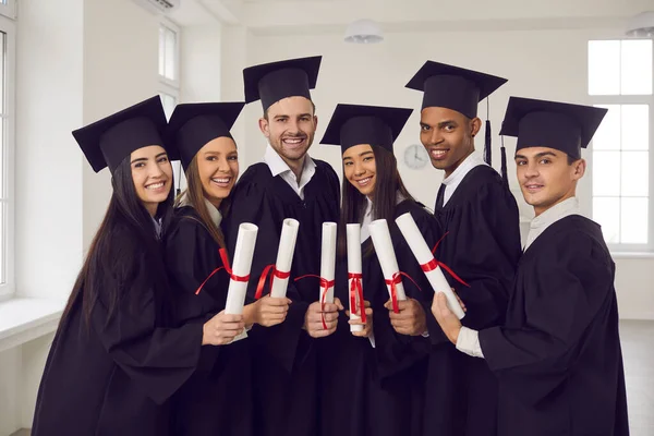 Boldog többnemzetiségű egyetemi diplomások csoportja fekete köpenyben, diplomával a kezükben — Stock Fotó