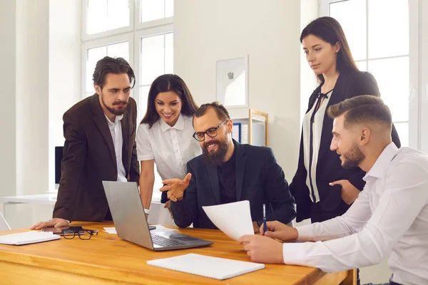 Team di uomini d'affari sorridenti seduti in ufficio intorno al computer portatile e discutendo di avvio — Foto Stock