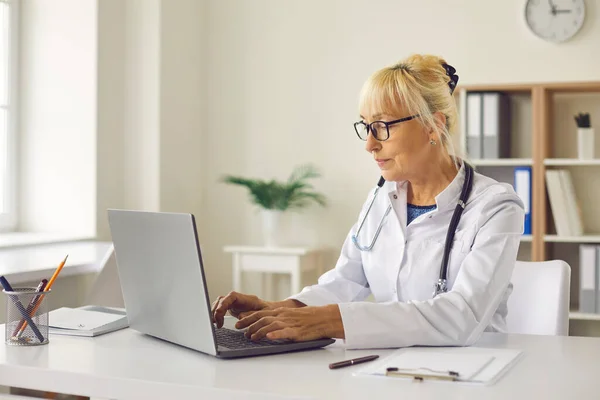 El médico se sienta frente a una computadora portátil e introduce el diagnóstico de los pacientes en una base de datos electrónica. — Foto de Stock
