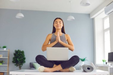 Genç Asyalı kadın mesai saatinde masada meditasyon yapıyor.