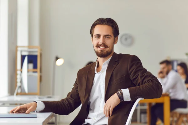 Handsome young business leader sitting at desk in office smiling and looking at camera — Stock Photo, Image