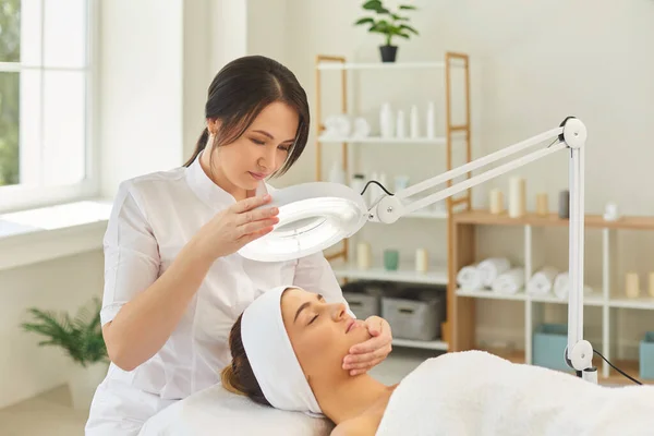 Dermatologue dirigeant la lampe vers le visage des femmes pendant le contrôle de la peau — Photo