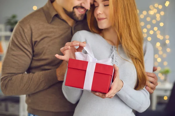 Krásný milující mladý pár žena a muž objímání a držení červené dovolené dárek box s dárkem — Stock fotografie