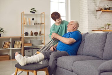 Torun, kırık bacağıyla kanepede oturan dedeye bir bardak su veriyor.