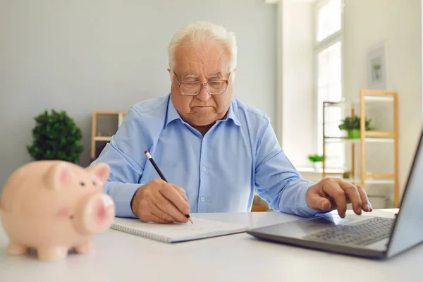 Gepensioneerde man met behulp van laptop en notities maken in notebook studeren pensioenplan en het beheer van zijn budget — Stockfoto