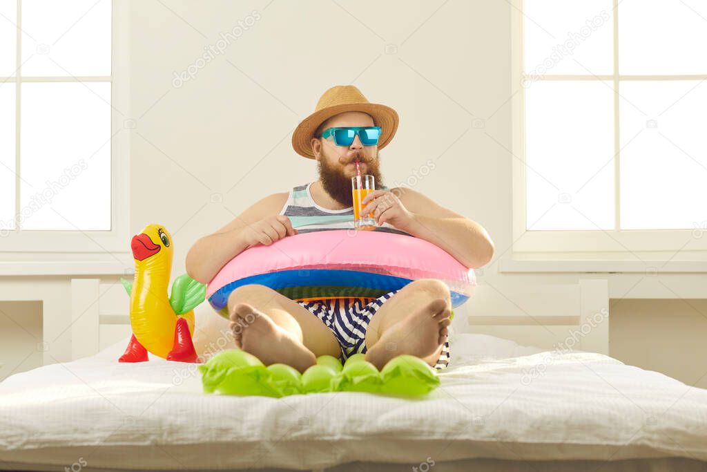 Funny barefoot young man in summer wear sipping beach cocktail in quarantine at home