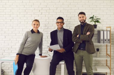 Üç mutlu iş adamından oluşan ekip kameraya bakıyor ve gülümsüyor.