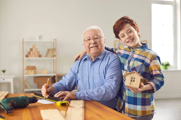 Gelukkig opa en kleinzoon hebben plezier en het maken van houten huis modellen in de werkplaats — Stockfoto