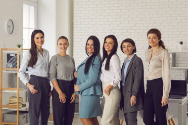 Bir grup mutlu, kendine güvenen genç iş kadını şirket ofisinde yan yana duruyor.