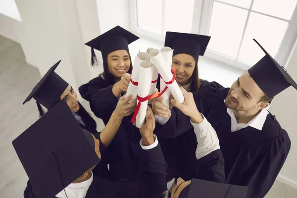 A végzősök felemelik a kezüket egy csomó diplomával, amik egy osztályteremben állnak az ablak mellett.. — Stock Fotó