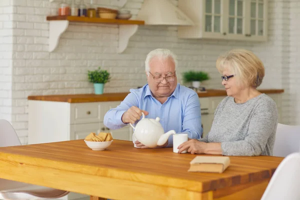 Heureux couple de grands-parents assis dans la cuisine, boire du thé avec des biscuits — Photo