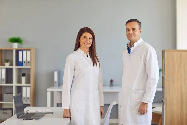 Trabajadores de la salud felices con batas de laboratorio de pie juntos en la oficina del hospital moderno —  Fotos de Stock