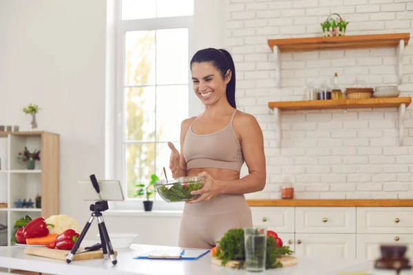 Cheerful fit vlogger filming culinary video, giving dieting tips and sharing healthy salad recipe