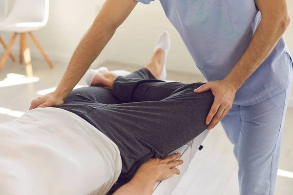 Ruce profesionálního muže osteopata fixace muž pacienti kolena a nohy klouby — Stock fotografie