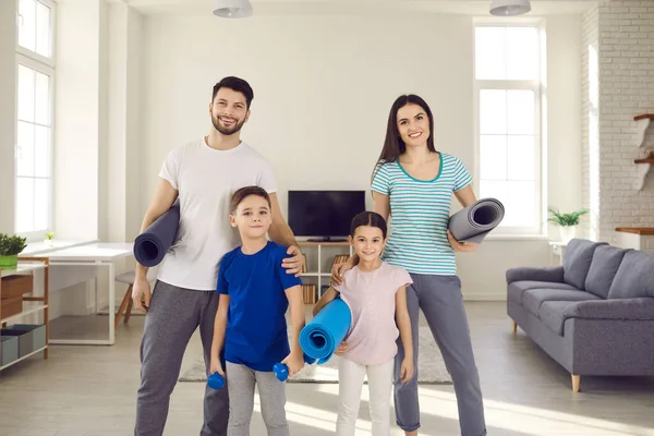 Família feliz com crianças segurando equipamentos esportivos e sorrindo para a câmera após o treino em casa — Fotografia de Stock