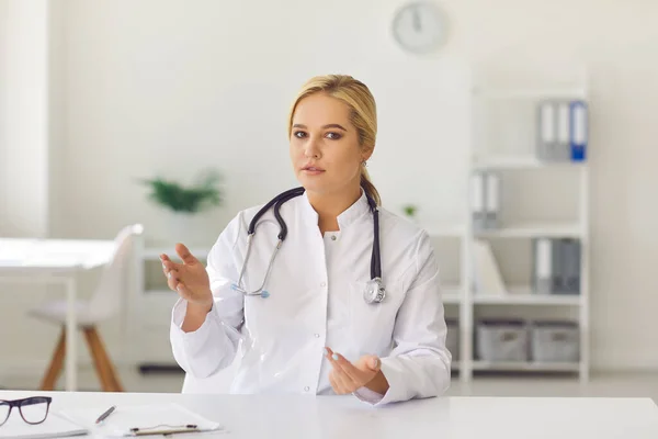 Junger Arzt sitzt im Büro am Schreibtisch, blickt in die Kamera und gibt Gesundheitsratschläge — Stockfoto