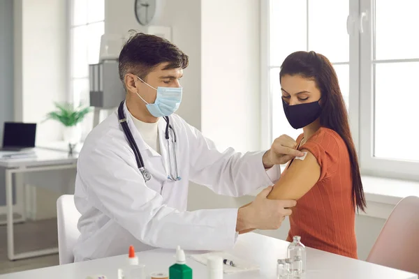 Médico en uniforme blanco y máscara médica pegando yeso estéril después de la inyección — Foto de Stock