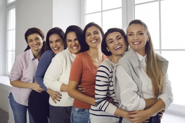 Team av glada unga kvinnor omfamnar varandra, ler och tittar på kameran — Stockfoto