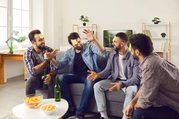 Teman-teman duduk di sofa di rumah dan bermain Who Am I guessing game dengan catatan post-it — Stok Foto