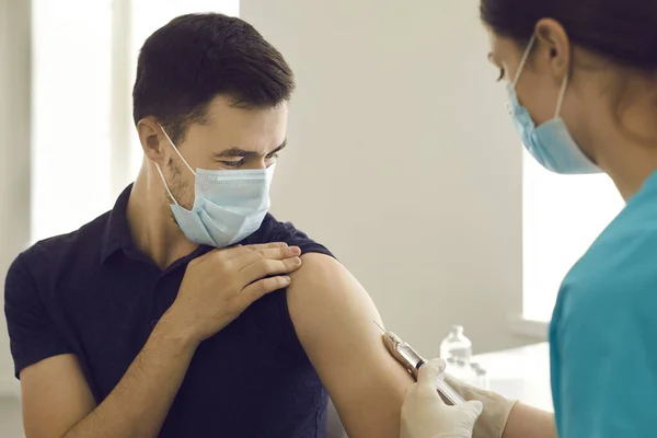 Man in face mask looking at syringe while getting Covid-19 vaccine at the clinic — Stock Photo, Image