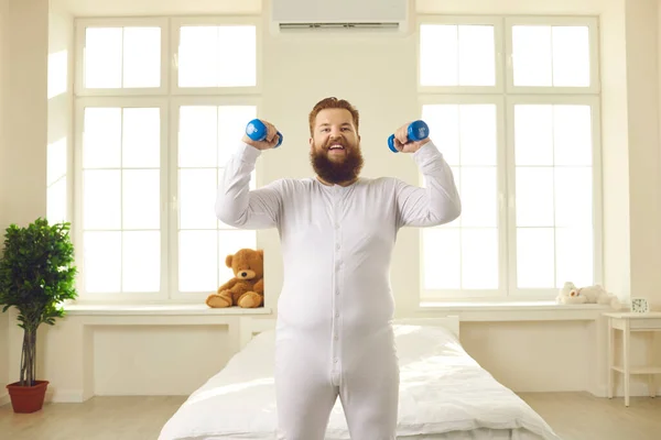 Feliz sorrindo jovem gordo em pijama fazendo exercício de fitness com halteres em casa — Fotografia de Stock