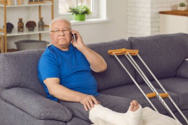 Kırık bacaklı son sınıf öğrencisi evdeki kanepede oturuyor ve akıllı telefondan arama yapıyor.