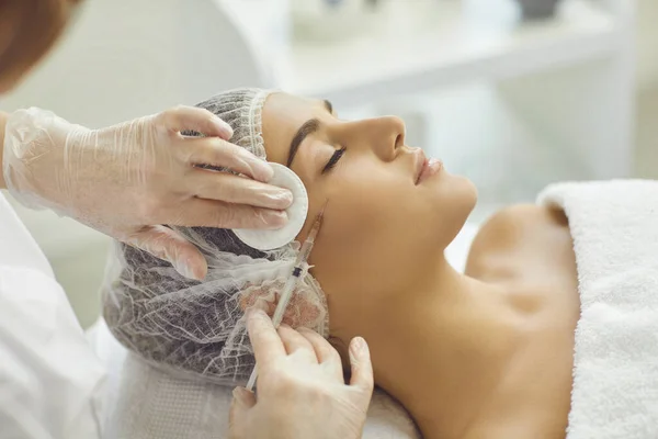 Kozmetik uzmanı, genç kadınların yanaklarına botoks yaparken pamuk pedlerle cilt siliyor. — Stok fotoğraf