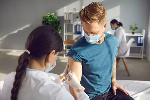 Tıbbi maskeli bir adam modern kliniğin güneşli ofisinde COVID-19 aşısı yaptırıyor. — Stok fotoğraf