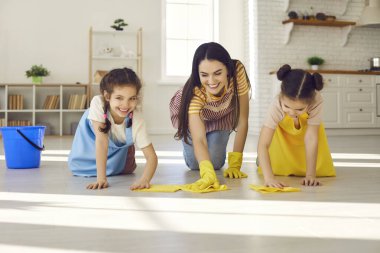 Mutlu genç bir anne ve büyüleyici küçük kızları birlikte yerleri siliyorlar.