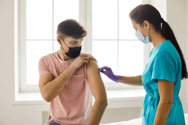 Enfermera desinfecta la piel en el brazo de los hombres jóvenes antes de darle Covid-19 o vacuna contra la gripe — Foto de Stock